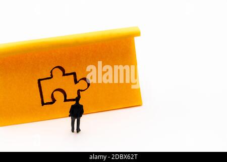 Figurine in miniatura posata come uomo d'affari davanti al pezzo di puzzle handrawn su carta adesiva nota, soluzione concetto immagine Foto Stock