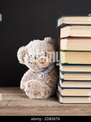 orsacchiotto di teddy che si stende da dietro una pila di libri, sfondo nero, ritorno a scuola Foto Stock