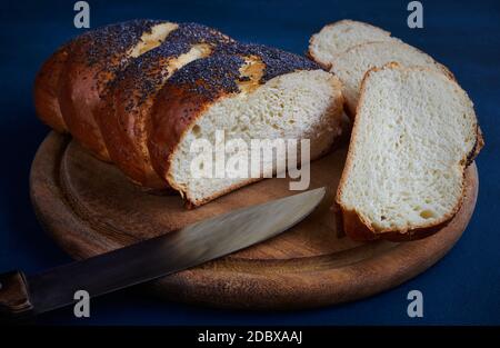 Pane bianco fresco cosparso di papavero su un tagliere con fette tagliate e un coltello, sfondo blu Foto Stock