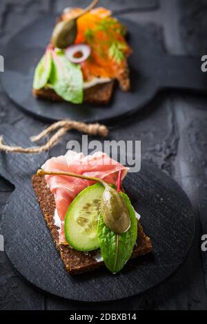 Variazione di panini sani aperti sul pane di Pumpernickel con verdure, salmone, prosciutto, erbe e formaggio morbido Foto Stock