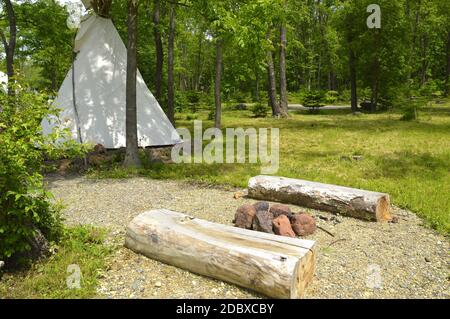 Due posti a sedere in legno fatti di bar accanto ad un falò Di pietre sullo sfondo del nativo americano wigwam in foresta Foto Stock