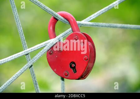 Lucchetto rosso a forma di cuore appeso sulle corde su sfondo verde Foto Stock