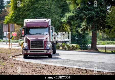 Carro lungo classico rosso scuro grande carro industriale semi-camion trattore con cabina bassa e semirimorchio a pianale piatto caricato le curve dalla strada principale a quella di riposo sono Foto Stock