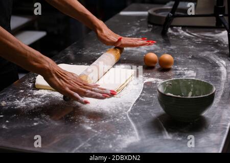 Lo chef prepara dolci in una cucina professionale. Impastare l'impasto. Uova, farina, tondino. Sfondo scuro. Foto Stock