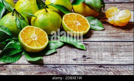 Mandarini verdi su vecchio sfondo di legno. Tangerini freschi mature, interi e verdi pelati con foglie, vista dall'alto o piatto. Spazio di copia per testo o disegno. Foto Stock