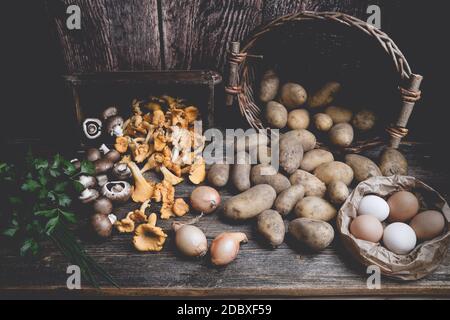 Patate, funghi, uova, prezzemolo, erba cipollina e cipolle su un tavolo di legno con burlap Foto Stock