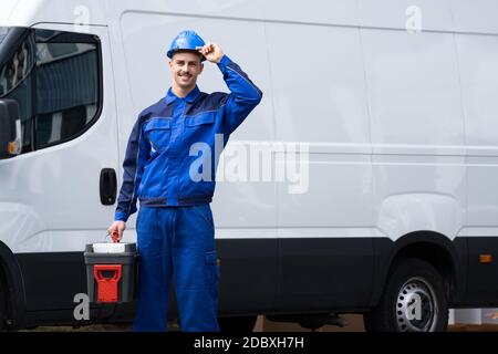Elettricista o idraulico felice con cassetta degli attrezzi vicino al veicolo a pulmino Foto Stock