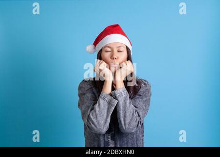 Mock su di una giovane donna asiatica seria e triste in un cappello di Babbo Natale mette la sua testa sulle sue mani clenched e soffia un bacio Foto Stock