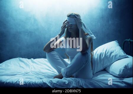 Donna psico bendata seduta a letto, camera oscura sullo sfondo. Donna psichedelica che ha problemi ogni notte, depressione e stress, Sadnes Foto Stock