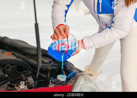 Donna in giacca sci versando auto antigelo del liquido del lavavetro in macchina sporca da antigelo blu contenitore d'acqua. Foto Stock