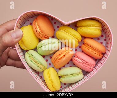 i macaron multicolore rotondi al forno si trovano in una scatola di cartone rosa a forma di cuore, vista dall'alto Foto Stock