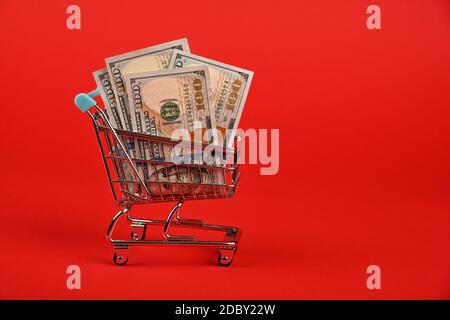 Primo piano diverse cento dollari US banconote in valuta cartacea nel piccolo carrello per lo shopping su sfondo rosso, vista laterale ad angolo basso Foto Stock