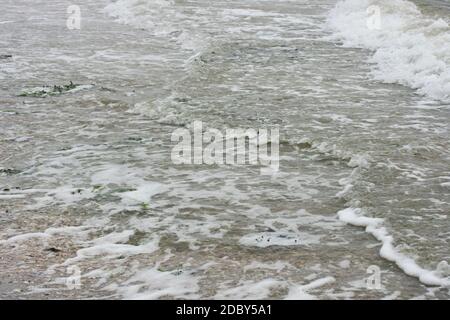 Onde con creste bianche inondare la spiaggia sabbiosa Foto Stock