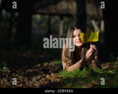 Giovane bella Brunette capelli lunghi Donna sdraiata nel Foresta con foglia di acero Foto Stock
