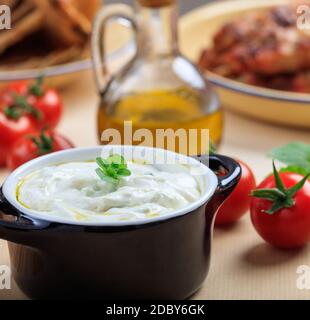 Salsa tzatziki greca. Antipasto tradizionale speziato a base di yogurt greco, cetriolo, olio d'oliva e aglio, servito in una ciotola nera vista guardaroba Foto Stock