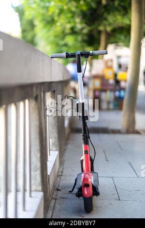 Scooter elettrico rosso parcheggiato e incatenato in modo sicuro a una recinzione. Eco-friendly moderno concetto di mobilità urbana moderna di condivisione dei trasporti con l'impianto elettrico Foto Stock