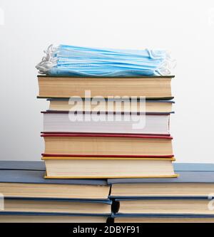 stack di vari libri e maschere mediche monouso su uno sfondo bianco, concetto di visitare le biblioteche in attrezzature di protezione personale durante quara Foto Stock