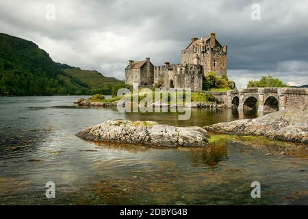 Sole splende attraverso le nuvole sul Castello Eilean Donan con rocce in primo piano loch. Dornie, Scozia Foto Stock