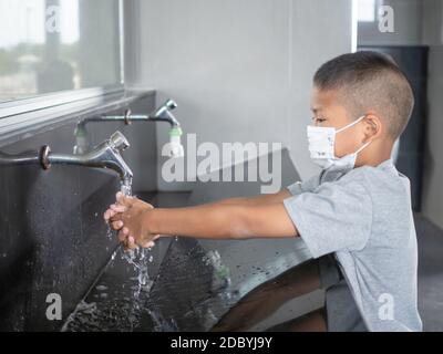 Ragazzo che indossa una maschera lavando le mani nei bagni pubblici Foto Stock