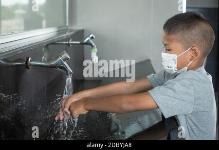 Ragazzo che indossa una maschera lavando le mani nei bagni pubblici Foto Stock