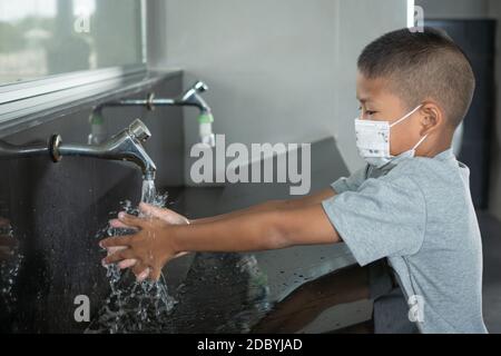 Ragazzo che indossa una maschera lavando le mani nei bagni pubblici Foto Stock