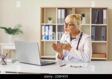 La dottoressa senior usa un computer portatile per condurre una consultazione online con il paziente. Foto Stock