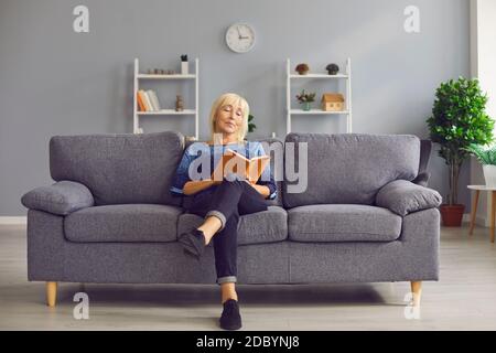 Ritratto di una donna senior focalizzata seduta su un divano e leggendo un libro interessante. Foto Stock