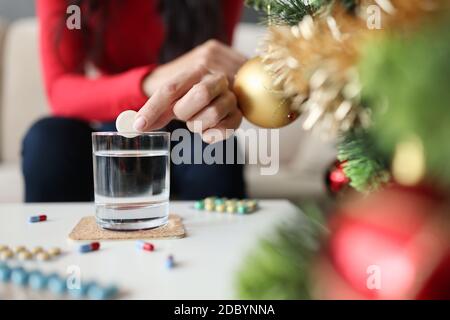 Mano femminile gettando compressa solubile effervescente in vetro di acqua Vicino albero di Natale Foto Stock