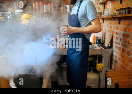 Il barista maschile in grembiule prepara il caffè aromatico in caffetteria. L'uomo prepara espresso fresco in caffetteria, cameriere al banco del bar Foto Stock