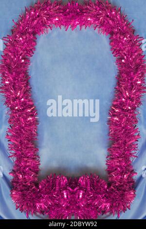 Bella cornice rosa con texture di Natale Tinsel su sfondo di tessuto di seta blu cobalto e spazio per inserire un testo. Foto Stock