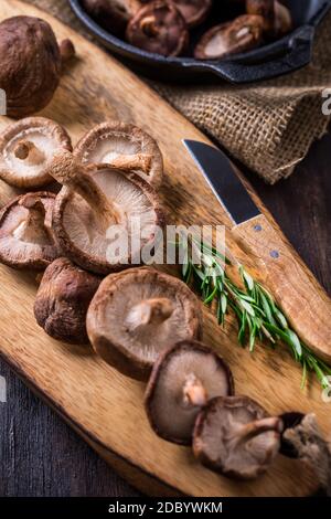 Deliziosi funghi Shiitake con rosmarino su tavola di legno da taglio. Foto Stock