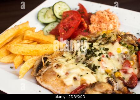 Pasto a base di carne di pollo con verdure diverse e patatine fritte servite su piatto bianco. Foto Stock