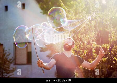 Il giocoso uomo bearded sta facendo enormi bolle di sapone sulla strada. Foto Stock