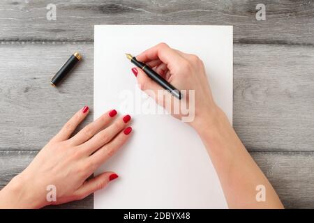 Vista da sopra alla donna di mani con unghie rosse, azienda fontana nero inchiostro della penna con pennino in oro, pronti a scrivere qualcosa sul vuoto pezzo di carta recante Foto Stock