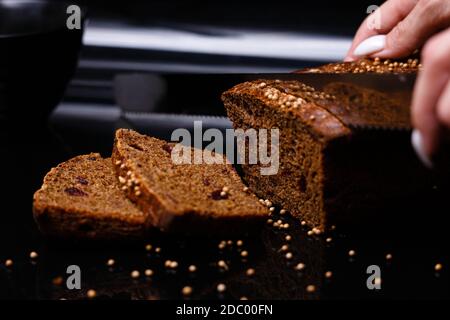 Pane nero fatto in casa su sfondo nero. Foto nella sezione. La ragazza taglia il pane con un coltello. Foto Stock