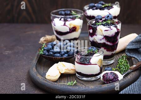 Dessert di mascarpone o ricotta, mirtilli e biscotto in vetro su sfondo scuro. Nessun cheesecake o tiramisù al forno. Foto Stock