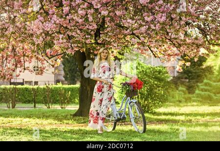 Stagione Sakura. Donna con bouquet di tulipani. Sakura albero in fiore. Giro romantico in bicicletta. Ragazza lungo abito retro Cruiser bicicletta sakura albero. Vacanze di primavera. Concetto di turismo. Trasporto e viaggio. Foto Stock