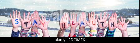 Bambini mani che tiene la parola inglese colorata rimanere sano. Neve Inverno sfondo con fiocchi di neve Foto Stock