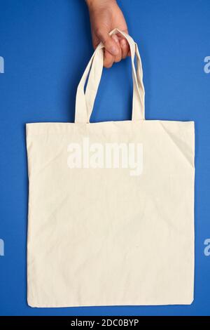 la mano femmina tiene una borsa di tessuto beige vuota vicino alle maniglie su uno sfondo blu, rifiuto di sacchetti di plastica, zero rifiuti Foto Stock