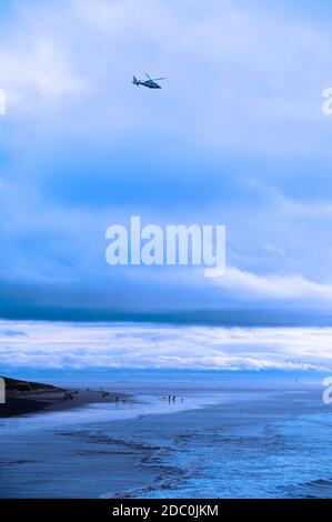 Camminatori di cani sulla spiaggia di St Annes su un buio freddo tardo pomeriggio in inverno con elicottero che vola in alto Foto Stock