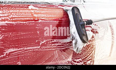 Auto rossa lavata in autoportante, dettaglio su pennello che lascia tratti sulla porta laterale, ampio banner con spazio vuoto per il testo a sinistra. Foto Stock