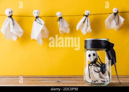 Divertente Halloween giorno decorazione partito, cute bianco fantasma artigianato spaventoso faccia appesa su sfondo hanno solo un fantasma bambino in vetro vaso, isolato giallo, Foto Stock