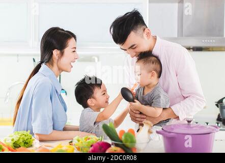 il genitore ed il ragazzo che alimentano il figlio un pezzo di carota dentro cucina Foto Stock