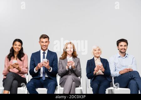 Sorridendo imprenditori multiculturali utilizzando smartphone isolati in grigio Foto Stock