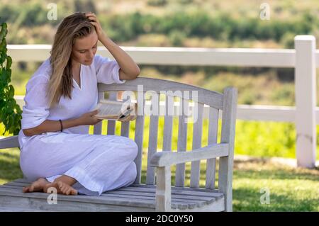 Bella giovane donna seduta sul banco nel Parco e leggendo un libro. Trascorrere una bella giornata estiva con la buona storia. Concetto di pace e relax. Foto Stock