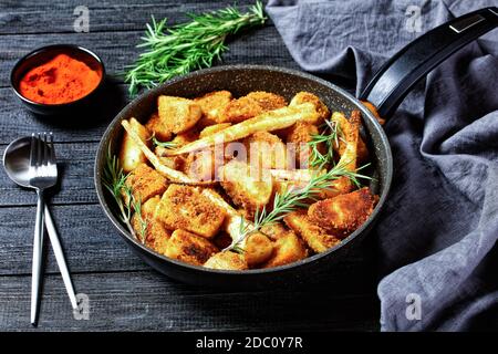 Verdure di radice al forno: Spicchi di patata e di pastinaca impanati con paprika affumicata e rametti di rosmarino fresco serviti su un backgrou di legno Foto Stock