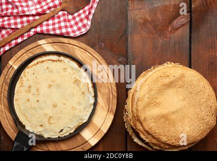 le sottili frittelle rotonde al forno sono impilate su un tavolo di legno, un tavolo marrone, vista dall'alto Foto Stock