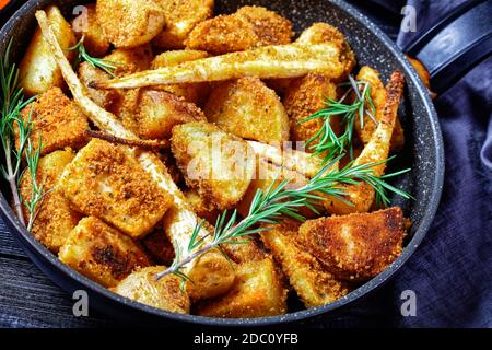 Verdure di radice al forno: Spicchi di patata e di pastinaca impanati con paprika affumicata e rametti di rosmarino fresco serviti su un backgrou di legno Foto Stock