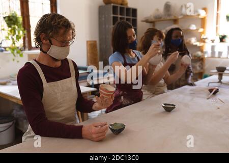 Gruppo multietnico di vasai in maschere facciali che lavorano in ceramica studio Foto Stock