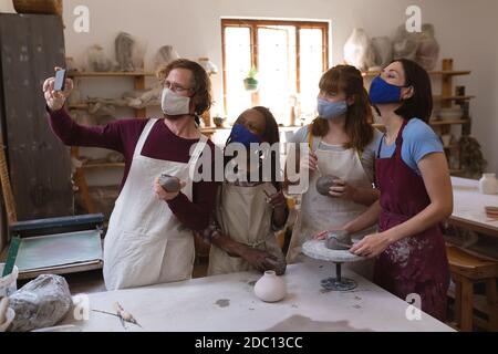 Gruppo multietnico di vasai in maschere facciali che lavorano in ceramica studio Foto Stock